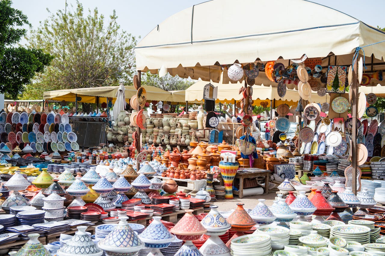 Stalls of assorted traditional dishes and plates with bright colors on local bazaar on sunny street with green trees in city